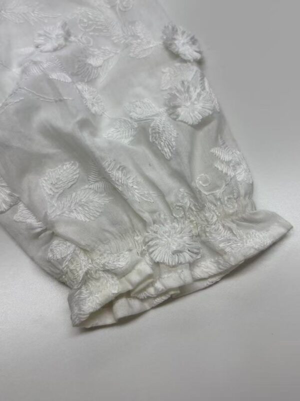 Close-up of white fabric with intricate floral embroidery and textured details, suitable for luxury fashion or bridal wear.