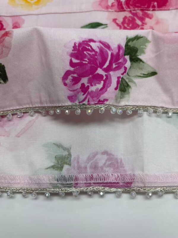 Close-up of floral fabric featuring pink and purple flowers with pearl embellishments along the edge, ideal for fashion and textile design.