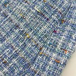 Close-up of vibrant multicolored tweed fabric showcasing intricate woven texture, ideal for high-end fashion garments and accessories.