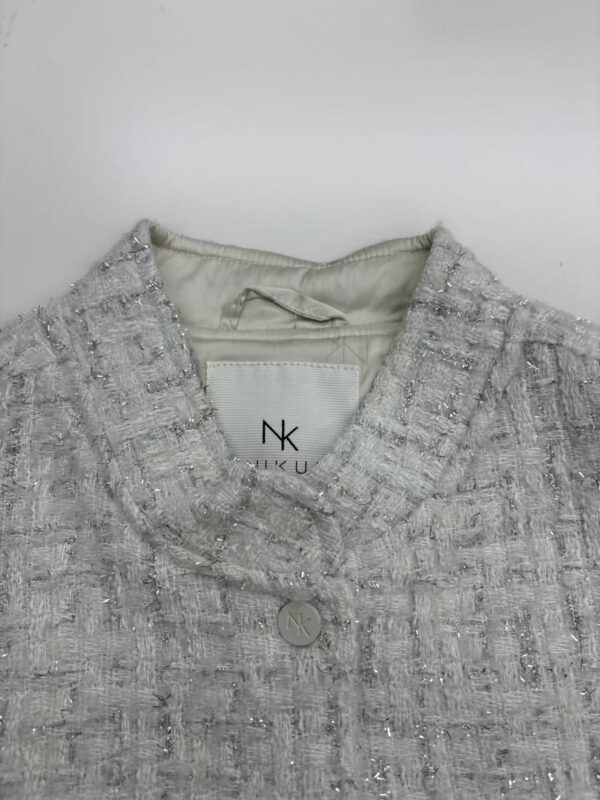 Close-up of a silver tweed women's jacket with a V-neckline and button closure, showcasing textured fabric and stylish design.