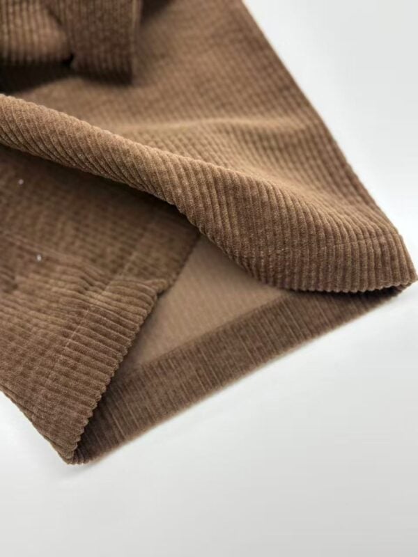 Close-up of brown corduroy fabric showing textured ridges and soft material, ideal for fashion and upholstery applications.