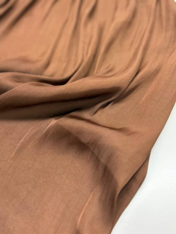 Close-up of soft, flowing brown fabric suitable for fashion and clothing design, showcasing smooth texture and gentle drapes.