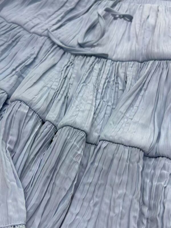 Close-up of a light blue pleated fabric dress with detailed stitching and texture, showcasing elegant and soft material suitable for fashion and apparel.