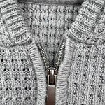 Close-up of a gray knitted sweater featuring a zipper closure, showcasing textured knitting patterns and a high collar for warmth and style.
