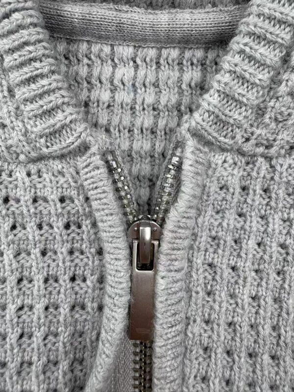 Close-up of a gray knitted sweater featuring a zipper closure, showcasing textured knitting patterns and a high collar for warmth and style.