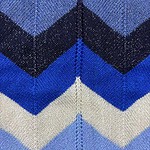 Close-up of blue and black chevron knit fabric with detailed stitching, ideal for stylish clothing and accessories.