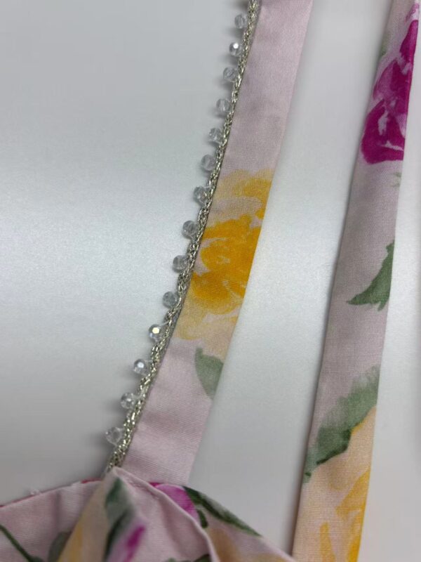 Close-up of a satin ribbon with floral print and decorative pearls, ideal for fashion accessories and garment embellishments.