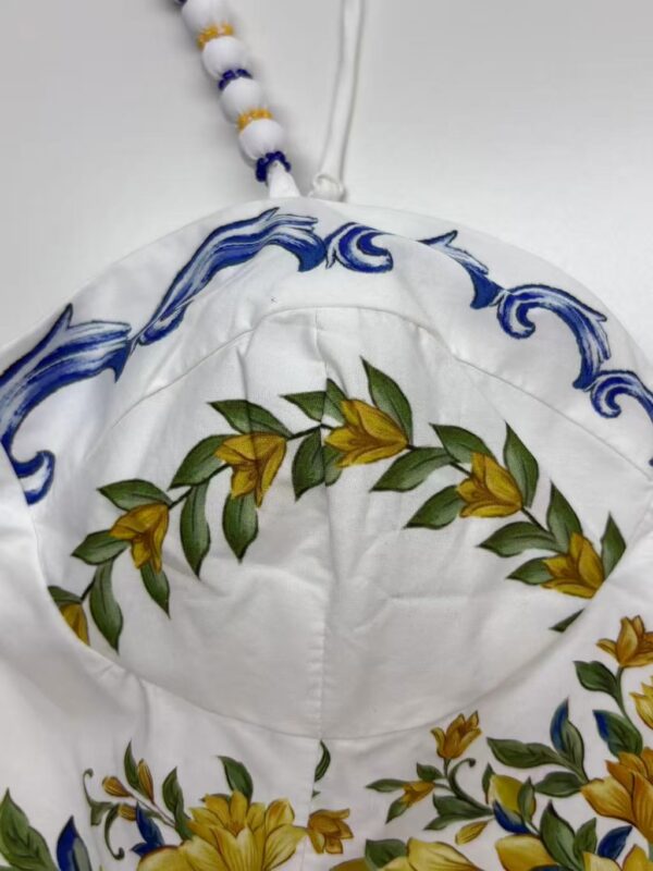 Close-up of a white hat with intricate floral embroidery in yellow and green, featuring blue decorative patterns and a beaded strap.