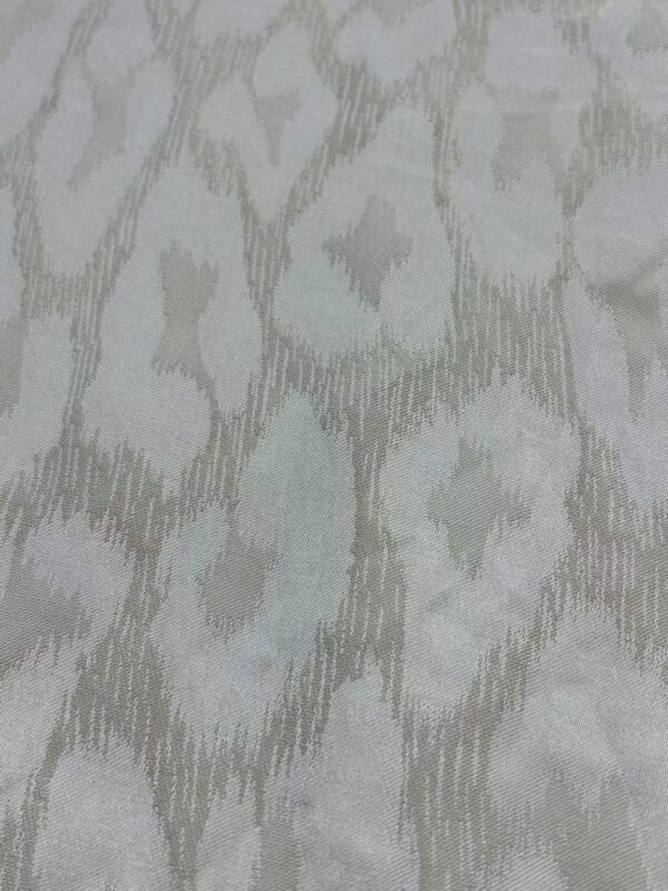 Close-up of a light-colored ikat fabric with intricate, abstract geometric design in soft neutral tones, ideal for stylish clothing and home decor.