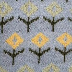 Close-up of a decorative carpet with geometric floral pattern in yellow, green, and gray colors.