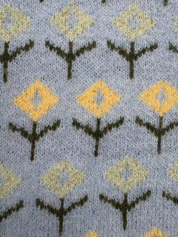 Close-up of a decorative carpet with geometric floral pattern in yellow, green, and gray colors.
