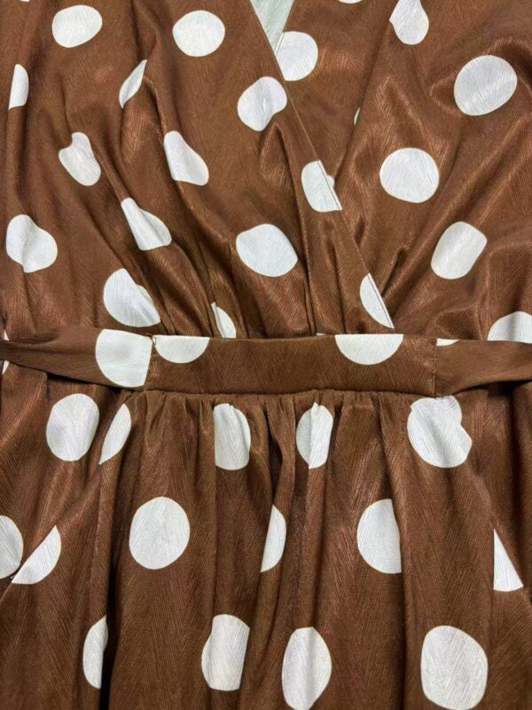 Close-up of a brown dress with white polka dots, featuring a gathered waist and fabric belt, perfect for casual or semi-formal occasions.