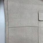 Close-up of beige fabric with a visible pocket and stitching, showcasing high-quality textile material suitable for fashion and apparel.