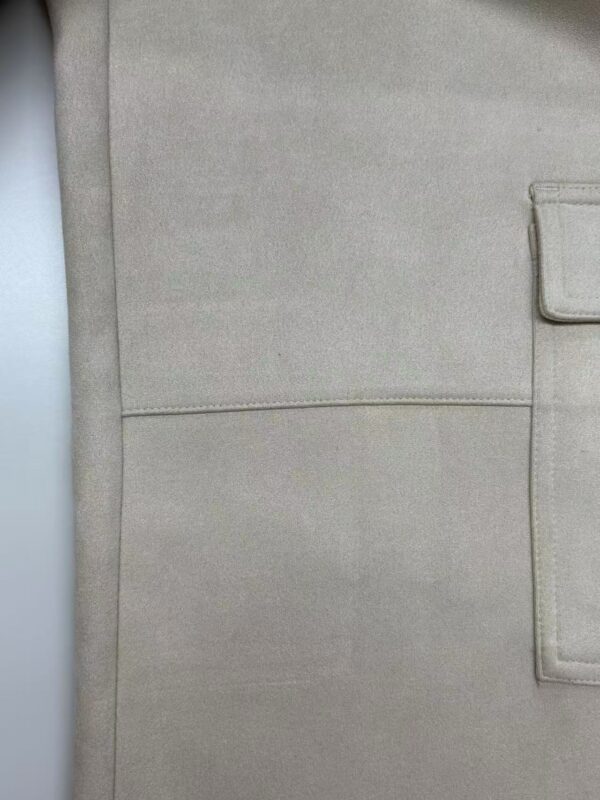 Close-up of beige fabric with a visible pocket and stitching, showcasing high-quality textile material suitable for fashion and apparel.