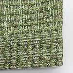 Close-up of a textured fabric with green, white, and purple threads woven in a detailed pattern.