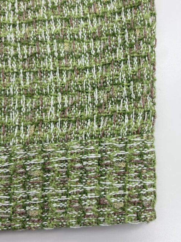 Close-up of a textured fabric with green, white, and purple threads woven in a detailed pattern.
