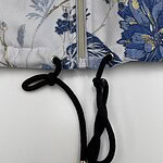 Close-up of a floral patterned jacket featuring a zipper and black drawstrings with gold tips, showcasing detailed embroidery and fabric texture.