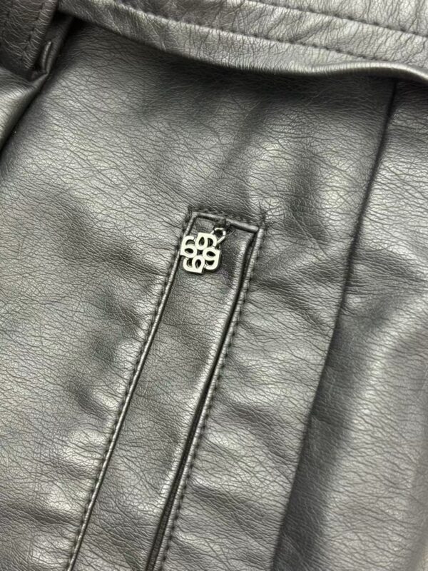 Detailed view of a black leather jacket with a silver zipper pull featuring a logo, showcasing the texture and craftsmanship of the material.