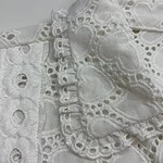 Close-up of intricate white embroidered fabric with eyelet and lace details, showcasing craftsmanship and delicate design.