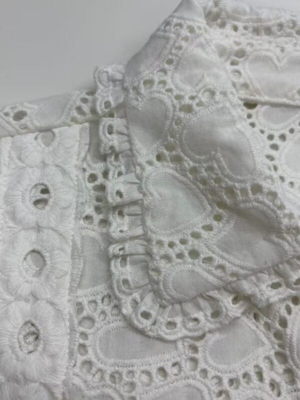Close-up of intricate white embroidered fabric with eyelet and lace details, showcasing craftsmanship and delicate design.