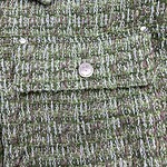 Close-up of green tweed fabric with multicolored threads and textured pattern, ideal for high-end fashion garments and accessories.
