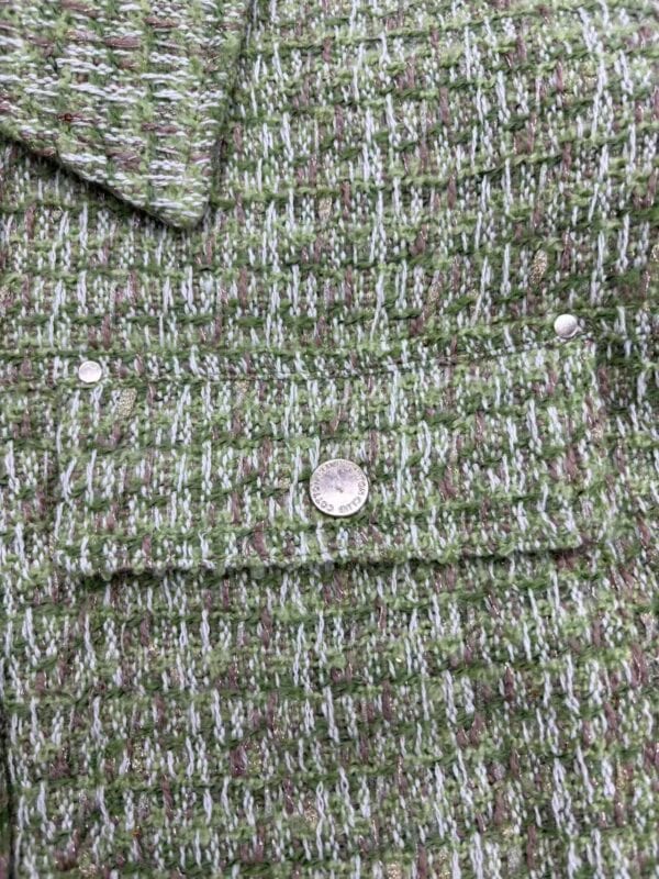 Close-up of green tweed fabric with multicolored threads and textured pattern, ideal for high-end fashion garments and accessories.