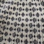 Close-up of a fabric with a black and white geometric pattern featuring diamonds and lines, pleated for a textured look.