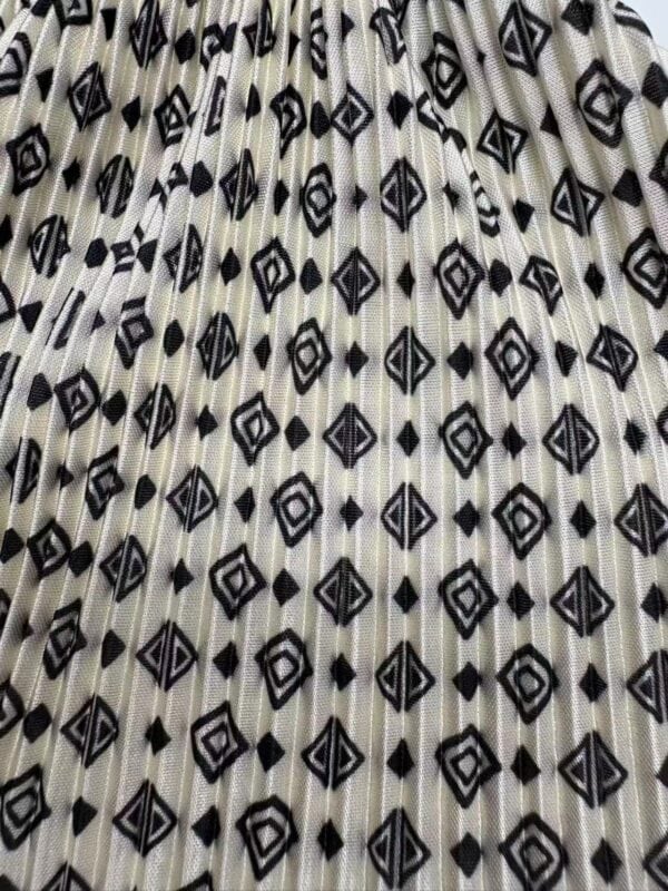 Close-up of a fabric with a black and white geometric pattern featuring diamonds and lines, pleated for a textured look.