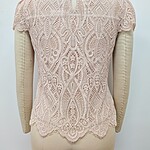 Close-up of a delicate pink lace women's top with intricate patterns and scalloped edges, displayed on a mannequin.
