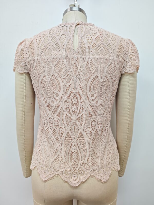 Close-up of a delicate pink lace women's top with intricate patterns and scalloped edges, displayed on a mannequin.