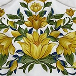 Detailed embroidery featuring yellow flowers and green leaves on white fabric, showcasing intricate craftsmanship and vibrant colors.