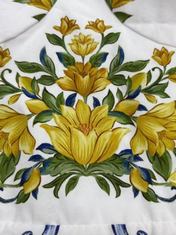 Detailed embroidery featuring yellow flowers and green leaves on white fabric, showcasing intricate craftsmanship and vibrant colors.