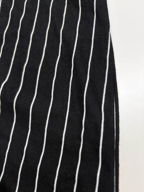 Close-up of black fabric with white vertical pinstripes, showcasing a stylish and classic pattern suitable for fashion apparel.
