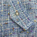 Close-up of a multicolored tweed fabric with a silver button, showcasing textured woven material with vibrant threads in blue, yellow, purple, and orange.