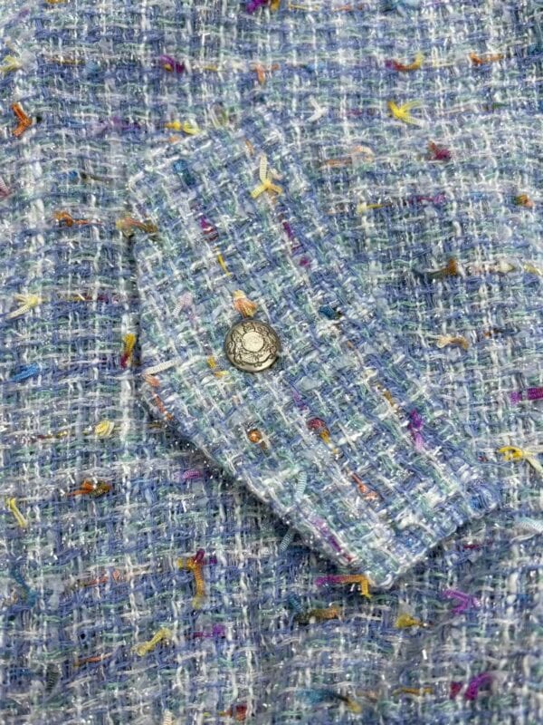 Close-up of a multicolored tweed fabric with a silver button, showcasing textured woven material with vibrant threads in blue, yellow, purple, and orange.