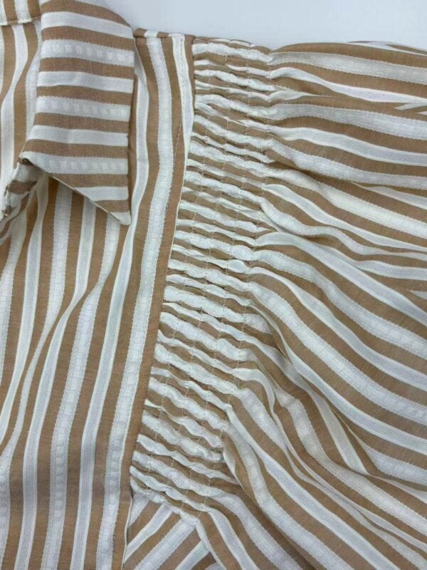 Close-up of a beige and white striped linen dress featuring a smocked waist and a collar, perfect for casual summer wear.