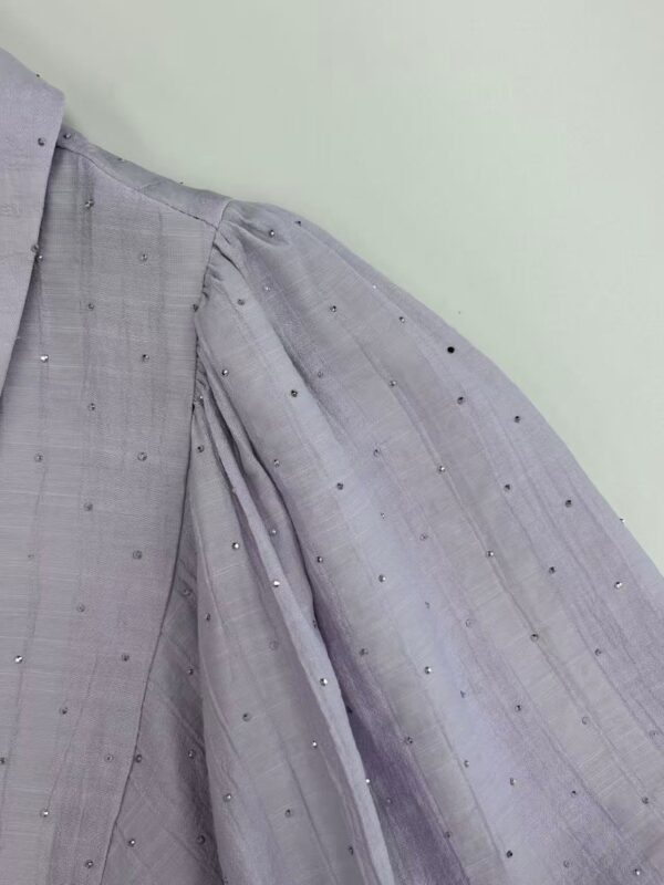 Close-up of a grey dress with intricate embroidery and small embellishments, showcasing fine fabric and detailed craftsmanship.