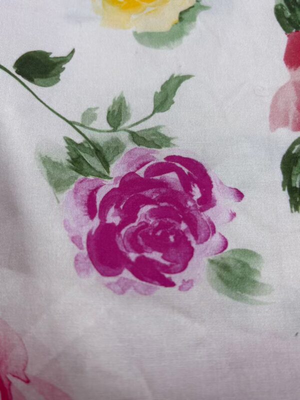 Close-up of a floral fabric with pink and green watercolor-style roses and leaves, ideal for fashion and home decor.