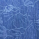 Close-up of blue fabric with intricate white embroidery pattern, showcasing detailed stitching and textured material for fashion and textile design.