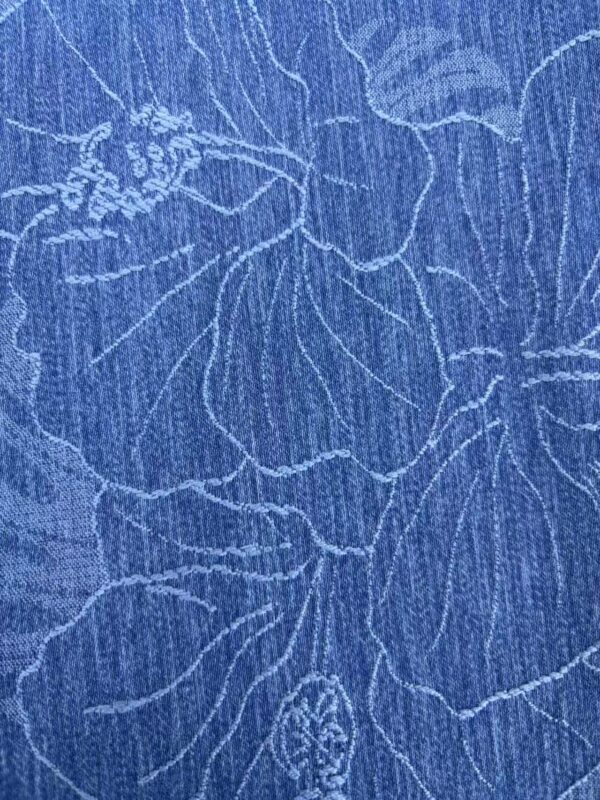 Close-up of blue fabric with intricate white embroidery pattern, showcasing detailed stitching and textured material for fashion and textile design.