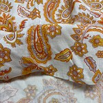 Close-up of paisley patterned fabric with orange, yellow, and white colors, showcasing intricate floral and paisley designs.