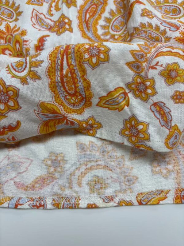 Close-up of paisley patterned fabric with orange, yellow, and white colors, showcasing intricate floral and paisley designs.