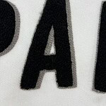 Close-up image of black embroidered letter A on white fabric, showcasing detailed stitching and texture, suitable for fashion or clothing product descriptions.