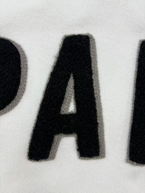 Close-up image of black embroidered letter A on white fabric, showcasing detailed stitching and texture, suitable for fashion or clothing product descriptions.
