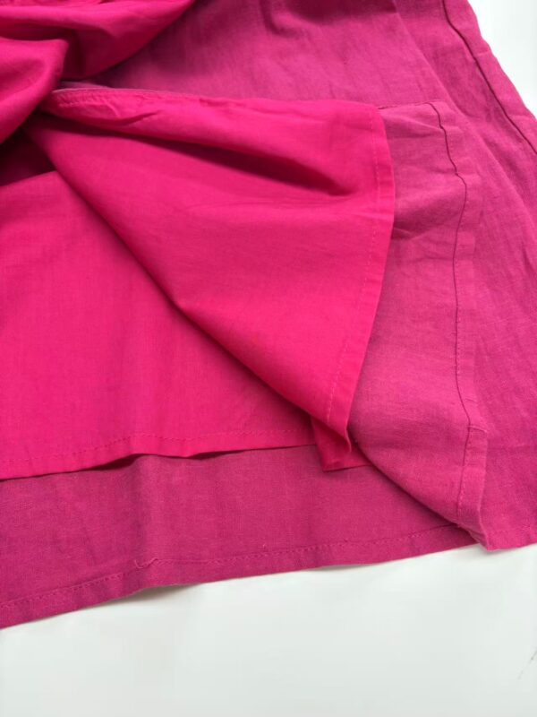 Close-up of vibrant pink linen fabric with detailed texture and stitching, showcasing high-quality material suitable for fashion and home decor.