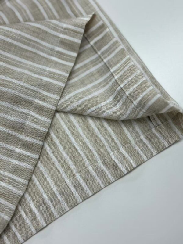 Close-up of beige striped linen fabric, showcasing its texture and pattern, ideal for fashion and home decor projects.