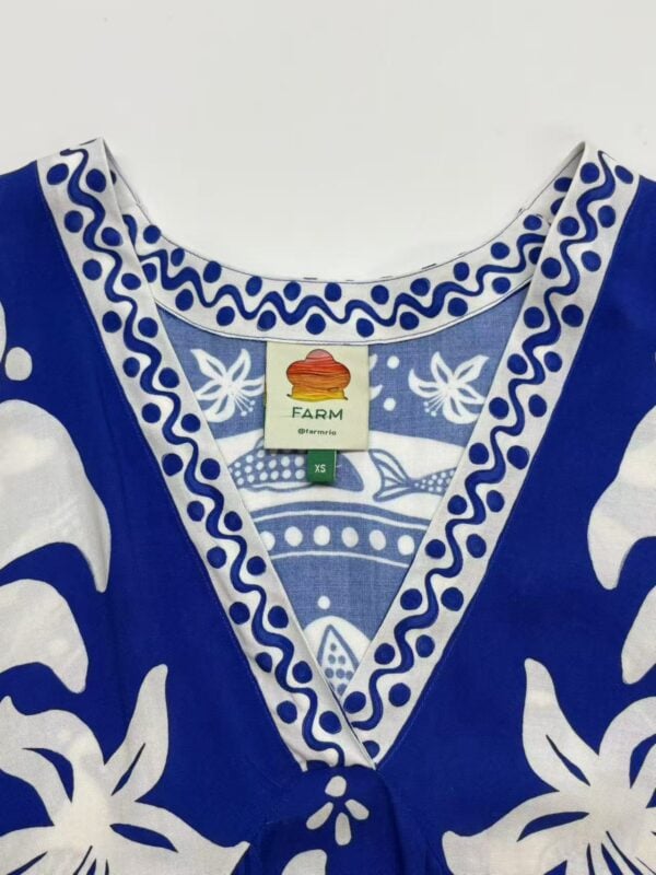 Close-up of a blue and white traditional dress with intricate patterns and embroidery, featuring a farm tag indicating size XS.