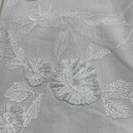 Close-up of white fabric with intricate floral embroidery, perfect for fashion and wedding dress designs.
