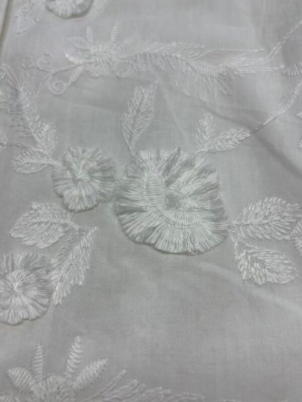 Close-up of white fabric with intricate floral embroidery, perfect for fashion and wedding dress designs.