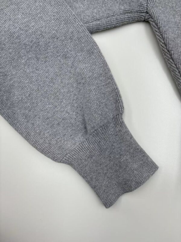 Close-up of a gray knit sweater sleeve showing detailed fabric texture and ribbed cuff.